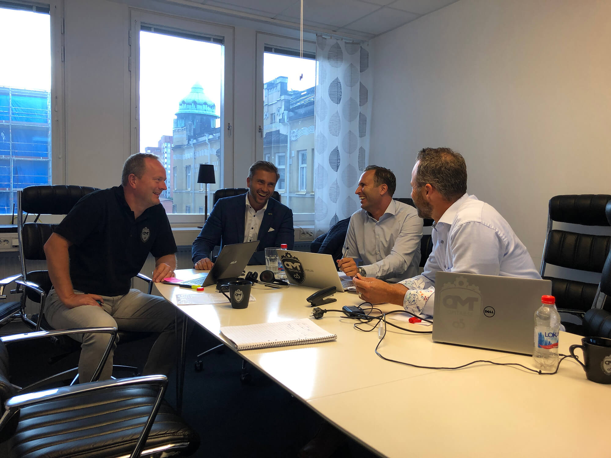 Personer sitter runt bord med datorer och skrattar